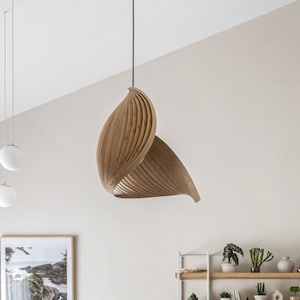 May include: A modern kitchen with a gray island and wooden accents. A large, sculptural wooden light fixture hangs above the island. Shelves with plants and decor are visible in the background. The room has a neutral color palette.