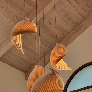 May include: A cluster of pendant lights with a unique design. Each light features a layered, curved shade in warm brown tones, suspended from the ceiling. The shades have a textured, ribbed appearance, and the light shines through the openings.