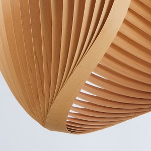 K&ouml;nnte beinhalten: Nahaufnahme eines Lampenschirms aus Holz mit einem geschwungenen, f&auml;cherartigen Design. Der Lampenschirm besteht aus d&uuml;nnen, hellbraunen Holzlatten.