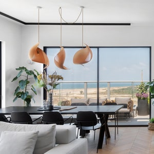 K&ouml;nnte beinhalten: Ein modernes Esszimmer mit einem Holztisch und schwarzen St&uuml;hlen. Der Raum hat gro&szlig;e Fenster mit Blick auf das Meer und einen Balkon. Drei h&ouml;lzerne Pendelleuchten h&auml;ngen &uuml;ber dem Tisch.