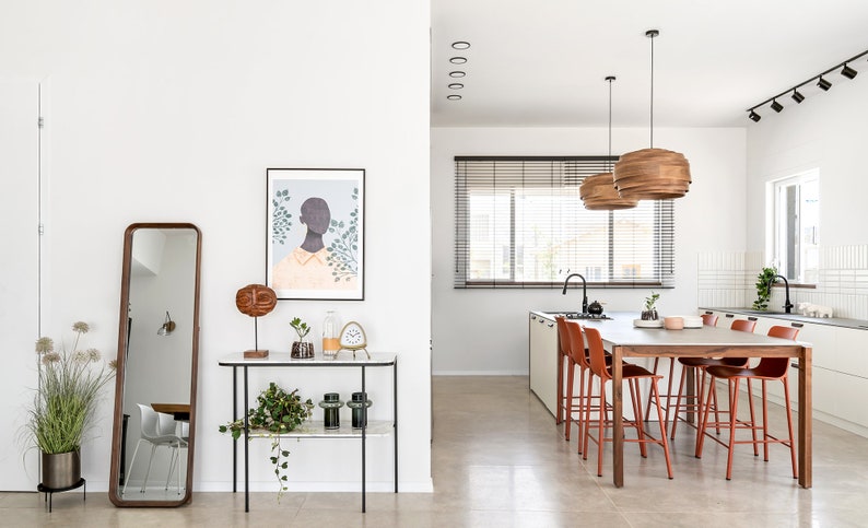 May include: A modern kitchen and dining area with white walls, a large window with blinds, a wooden dining table with six red chairs, and a black and white art print on the wall.
