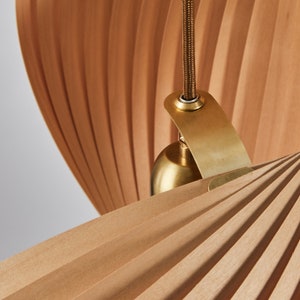K&ouml;nnte beinhalten: Nahaufnahme einer Holz-Pendelleuchte mit einem Messingbaldachin und einem Kabel. Die Leuchte hat ein gefaltetes, f&auml;cherf&ouml;rmiges Design.