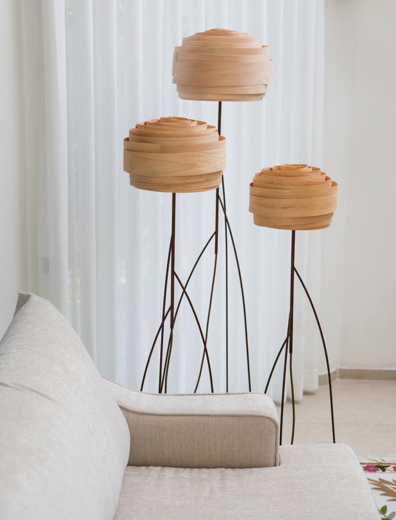 May include: Three wooden floor lamps with a unique design. The lamps have a round, layered shade made of wood and a thin black metal base.