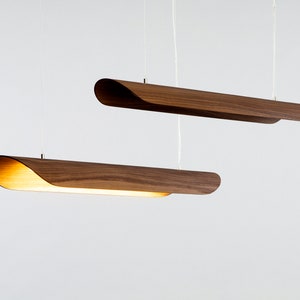 Op de afbeelding: Twee houten hanglampen met een gebogen ontwerp hangen aan het plafond tegen een witte achtergrond.