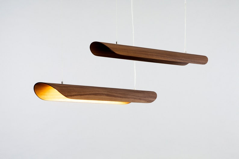 Op de afbeelding: Twee houten hanglampen met een gebogen ontwerp hangen aan het plafond tegen een witte achtergrond.