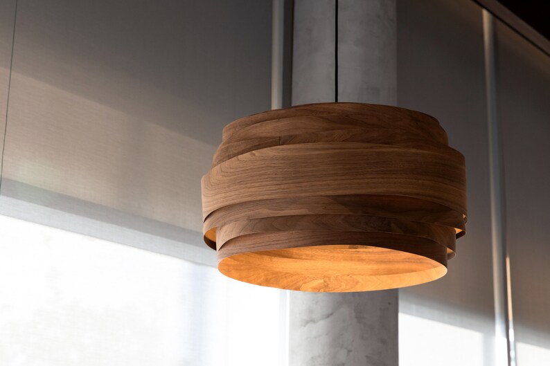 May include: A wooden pendant light fixture with a layered design. The light is on and emits a warm glow.