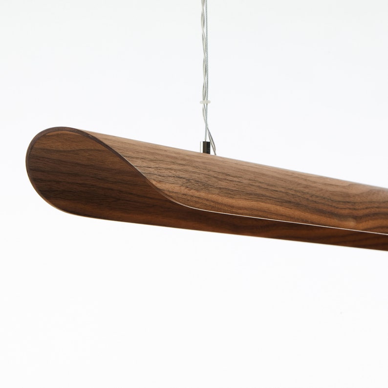Op de afbeelding: Een lange, houten hanglamp met een gebogen, walnootkleurige kap.
