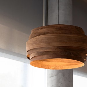 May include: A contemporary wooden pendant light, suspended from a black cable. The light fitting is constructed from multiple layers of curved wood, creating a distinctive, open design. The warm light shines from within, highlighting the natural wood grain.