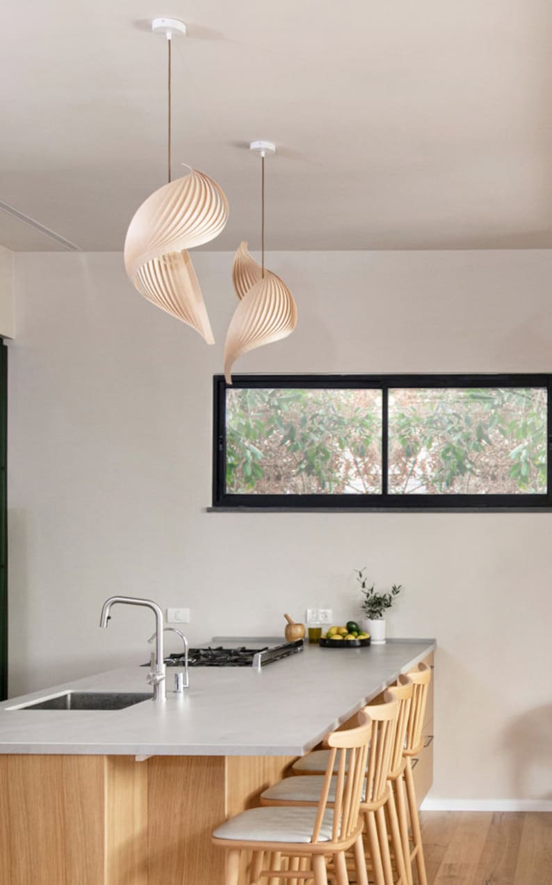 K&ouml;nnte beinhalten: Eine moderne K&uuml;che mit einer wei&szlig;en Arbeitsplatte und Holzschr&auml;nken. Es gibt vier Holzbarhocker und einen Wasserhahn aus Edelstahl. Die K&uuml;che hat ein gro&szlig;es Fenster mit Blick auf B&auml;ume und eine einzigartige Holzleuchte, die von der Decke h&auml;ngt.