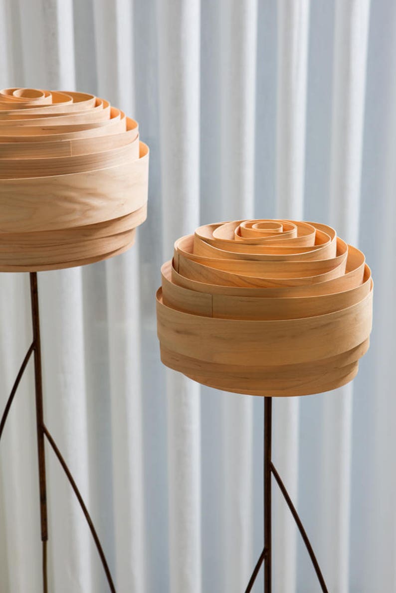 May include: Two wooden lamps with a unique, layered, rose-like design. The lamps are on tall, thin, black metal stands.