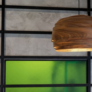 May include: A wooden pendant light fixture with a layered design hangs from the ceiling against a backdrop of gray and green walls.