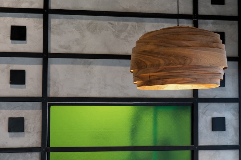 May include: A wooden pendant light fixture with a layered design hangs from the ceiling against a backdrop of gray and green walls.
