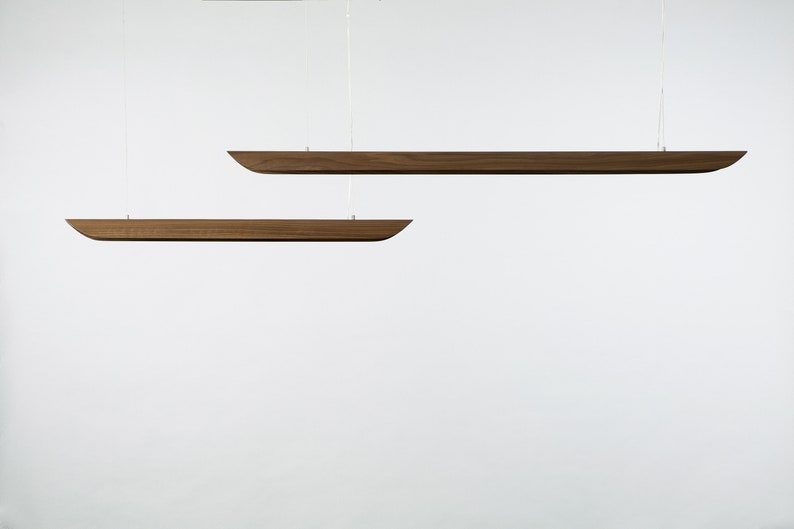 Op de afbeelding: Twee houten hanglampen die aan het plafond hangen. De lampen zijn lang en smal, met een licht gebogen vorm. Ze zijn gemaakt van donker hout.