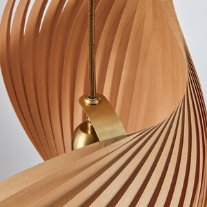 May include: A modern pendant light fixture with a unique design. The light features a spiraling shade made of thin, light brown wooden slats. A brass-colored metal fixture and cord support the light.