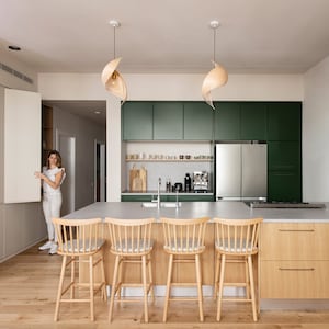 K&ouml;nnte beinhalten: Eine moderne K&uuml;che mit gr&uuml;nen Schr&auml;nken, einem K&uuml;hlschrank aus Edelstahl und einer gro&szlig;en Insel mit vier Holzbarhockern. Die Insel hat eine hellgraue Arbeitsplatte und eine Holzbasis. Die K&uuml;che hat einen Holzboden und ein gro&szlig;es Fenster mit Blick nach drau&szlig;en.