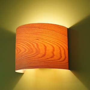 May include: A wooden wall sconce with a cylindrical shade. The shade has a wood grain pattern and is lit from within, casting a warm glow.