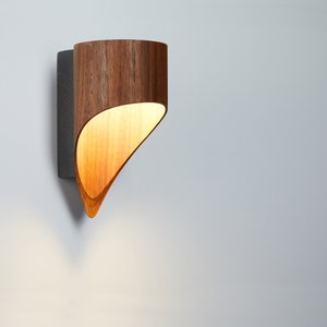 May include: A wooden wall sconce with a curved, light-colored shade. The sconce is mounted on a white wall.