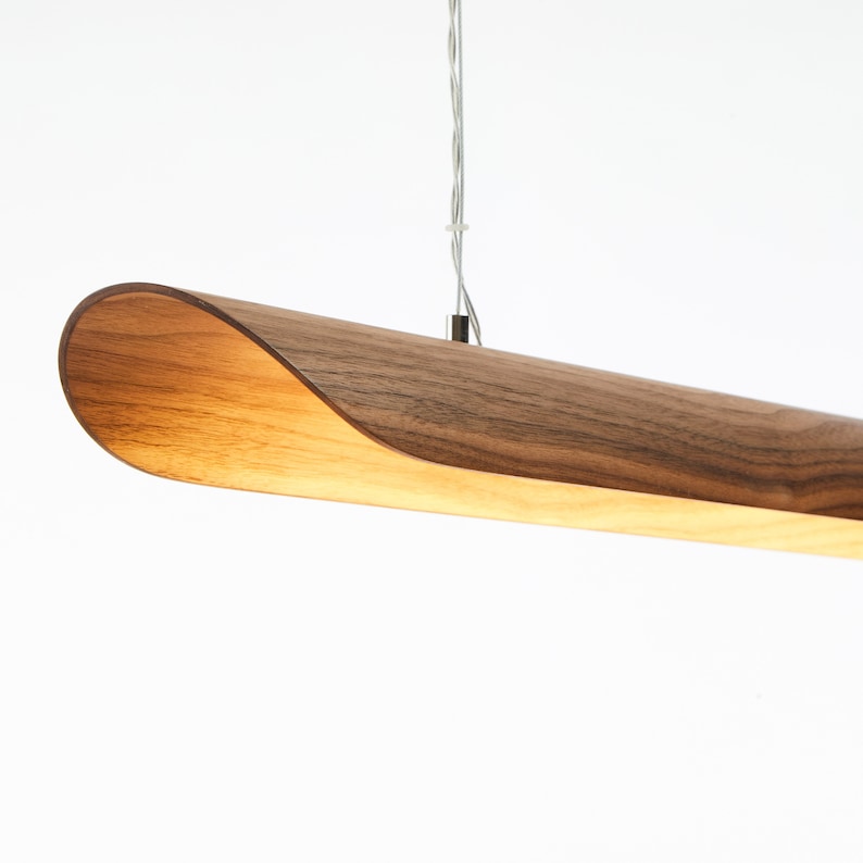 Op de afbeelding: Een moderne hanglamp van walnoot hout met een gebogen ontwerp. De lamp hangt aan een dunne draad.