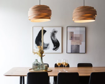May include: A dining room table with six chairs, two wooden pendant lights, and two framed abstract art prints. The table is made of wood and has a light brown finish. The chairs are black with black legs. The pendant lights are made of wood and have a light brown finish. The art prints are black and white and have a modern design.