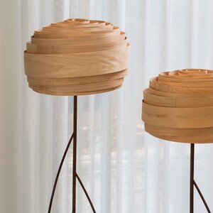 May include: Two wooden floor lamps with layered shades. The shades are made of thin, light wood and are stacked in a circular pattern. The lamps are on a white background.