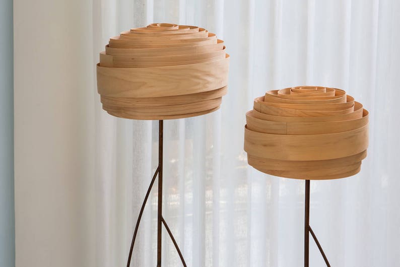 May include: Two wooden floor lamps with layered shades. The shades are made of thin, light wood and are stacked in a circular pattern. The lamps are on a white background.