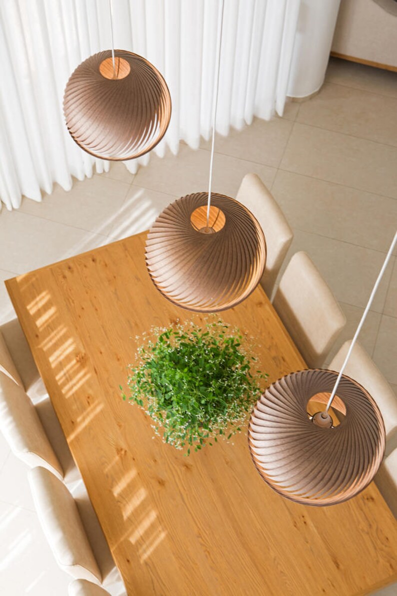 K&ouml;nnte beinhalten: Drei braune Holz-Pendelleuchten h&auml;ngen &uuml;ber einem Holz-Esstisch mit einer gr&uuml;nen Pflanze in der Mitte. Die Leuchten haben ein einzigartiges Spiraldesign.