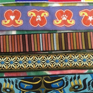 May include: Close-up of several decorative ribbons. The ribbons feature various designs, including colorful stripes, repeating cartoon dog-like figures, floral patterns, and bear claw motifs. The color palette includes blue, green, orange, and brown.