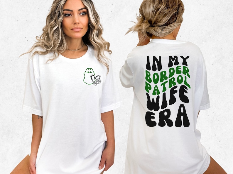 May include: White t-shirt with a green border patrol badge and flowers on the left chest. The back of the shirt has the text "In My Border Patrol Wife Era" in green and black.
