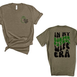 May include: A green and black t-shirt with the text "In My Border Patrol Wife Era" on the back. The front of the shirt has a small green and black graphic of a badge with a heart.