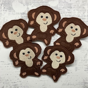 May include: Five brown felt monkey appliques with embroidered details. Each monkey has a smiling face, brown eyes, and a beige body.