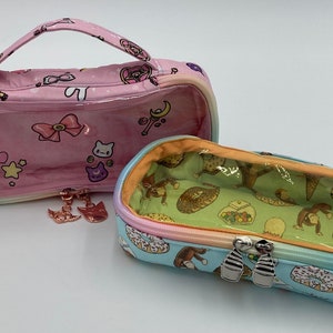 May include: Two clear zippered pouches with colorful rainbow trim. The pink pouch has a clear window and a small handle. The blue pouch has a clear window and a monkey and donut pattern.