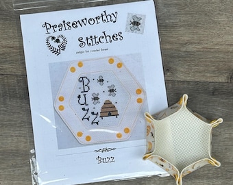 May include: A white and yellow cross-stitch pattern with a beehive and bees, titled "Buzz" from Praiseworthy Stitches, a design for counted thread. The pattern is packaged with a white and yellow hexagonal fabric pouch.