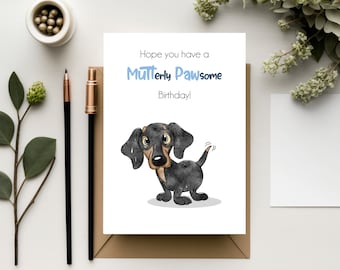 May include: A birthday card featuring a cartoon dachshund. The card's text reads "Hope you have a Mutt-erly Pawsome Birthday!" The dachshund is black and brown. The card is on a brown envelope, with a pen and decorative items.