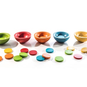 Peut inclure: Un ensemble de cinq bols en bois de diff&eacute;rentes couleurs, notamment vert, rouge, orange, bleu et jaune. Les bols sont dispos&eacute;s en rang&eacute;e et plusieurs petits disques en bois sont &eacute;parpill&eacute;s autour d'eux dans des couleurs assorties.