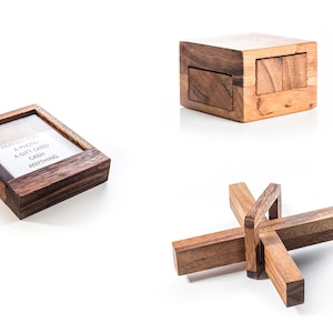 Puede incluir: Tres cajas de rompecabezas de madera. La primera caja es una caja cuadrada pequeña con una tapa deslizante. La segunda caja es una caja cuadrada más grande con una tapa deslizante. La tercera caja es una caja en forma de estrella con una tapa deslizante. Las tres cajas están hechas de madera oscura.