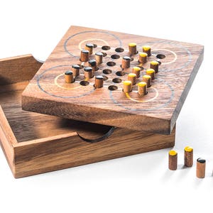 May include: A wooden game board with a grid of holes and yellow and black pegs. The board is open and the lid is beside it. The lid is also made of wood and has a natural finish.