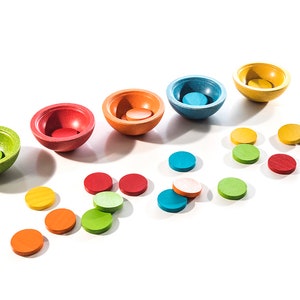 Peut inclure: Un ensemble de six bols en bois color&eacute;s avec des disques de couleur assortis. Les bols sont dispos&eacute;s en arc-en-ciel, du vert au jaune. Les disques sont dispers&eacute;s autour des bols.