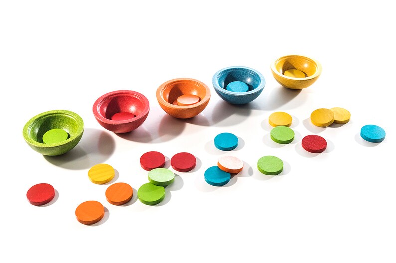 Peut inclure: Un ensemble de six bols en bois color&eacute;s avec des disques de couleur assortis. Les bols sont dispos&eacute;s en arc-en-ciel, du vert au jaune. Les disques sont dispers&eacute;s autour des bols.