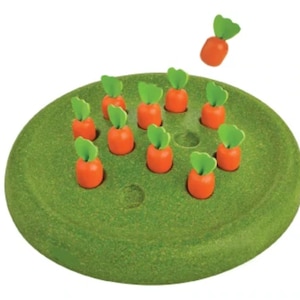 May include: A green wooden game board with 12 orange carrot-shaped pieces with green tops. One carrot piece is in the air above the board.