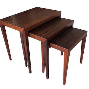 May include: A set of three nesting tables made of dark wood with a rich grain pattern. The tables are rectangular and have a simple, modern design.