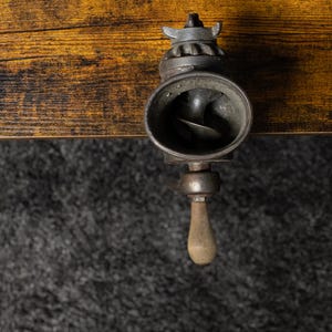 May include: A vintage metal hand crank grinder with a black finish and a wooden handle. The grinder has a round opening with a metal blade inside.