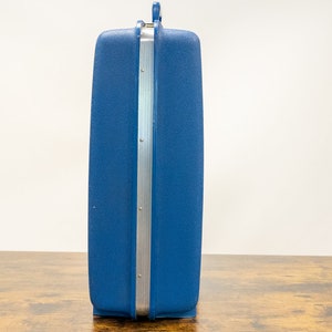 May include: A blue hard-sided suitcase with a silver trim and a handle.