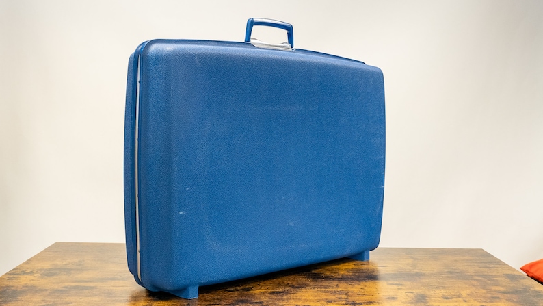 May include: A blue hard-sided suitcase with a handle on top.