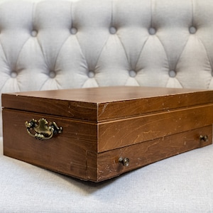 May include: A wooden box with a hinged lid and a drawer. The box has a brass handle and two brass knobs. The box is sitting on a light gray tufted sofa.