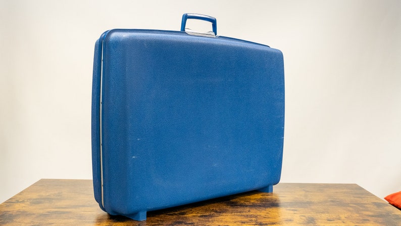 May include: A blue hard-sided suitcase with a handle on top.