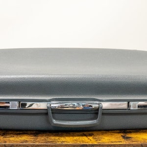 May include: A gray hard-sided suitcase with a silver handle and two silver latches.