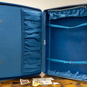 May include: Open blue suitcase with a blue fabric lining and multiple pockets. The suitcase has a zipper closure and two straps inside.