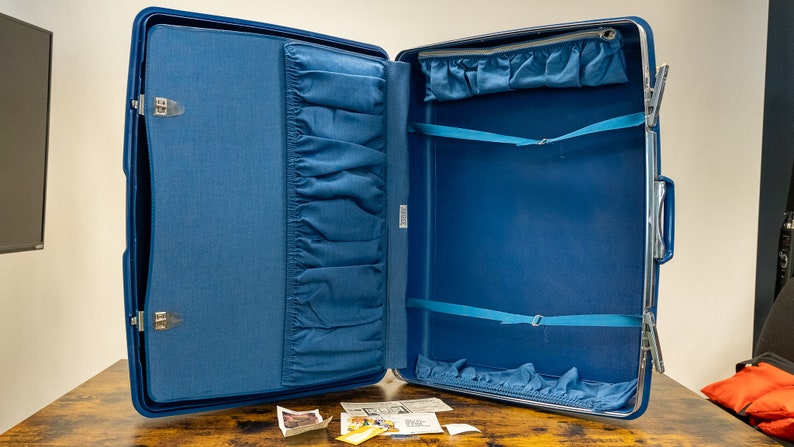 May include: Open blue suitcase with a blue fabric lining and multiple pockets. The suitcase has a zipper closure and two straps inside.