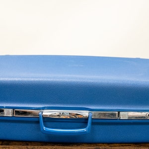 May include: A blue hard-sided suitcase with a silver handle and a silver lock.