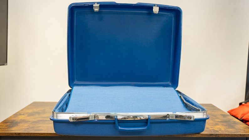May include: An open blue suitcase with a light blue lining. The suitcase has a silver handle and two silver latches.